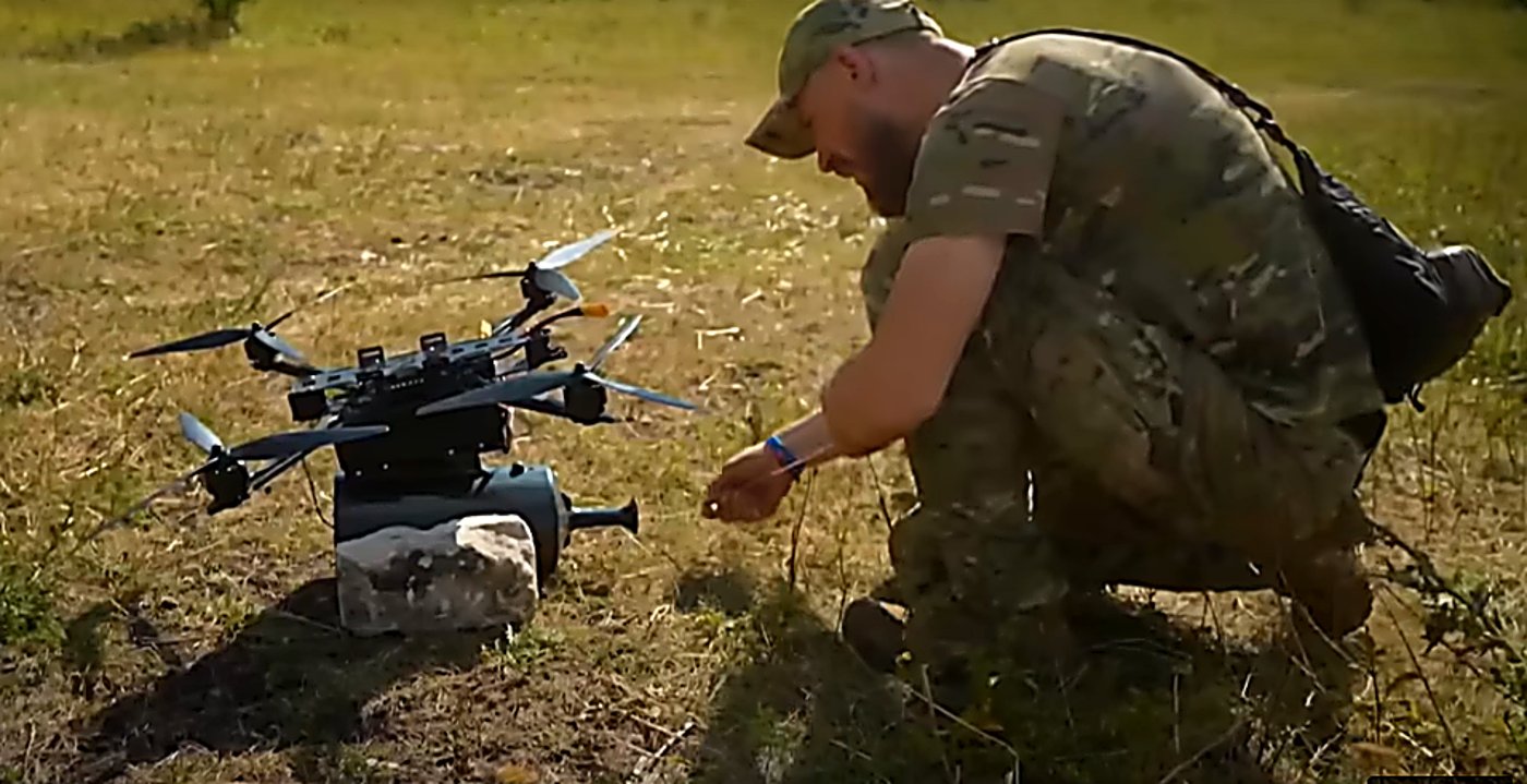 לוחם בשטח פתוח כורע ליד רחפן כבד מסוג FPV עם כבל סיב אופטי שנמתח לאורך 41 ק"מ