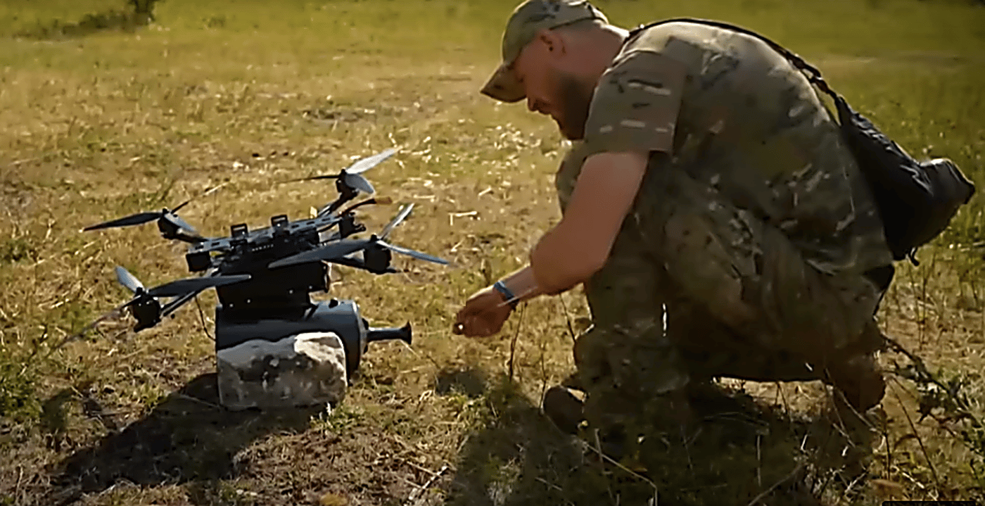 לוחם בשטח פתוח כורע ליד רחפן כבד מסוג FPV עם כבל סיב אופטי שנמתח לאורך 41 ק"מ